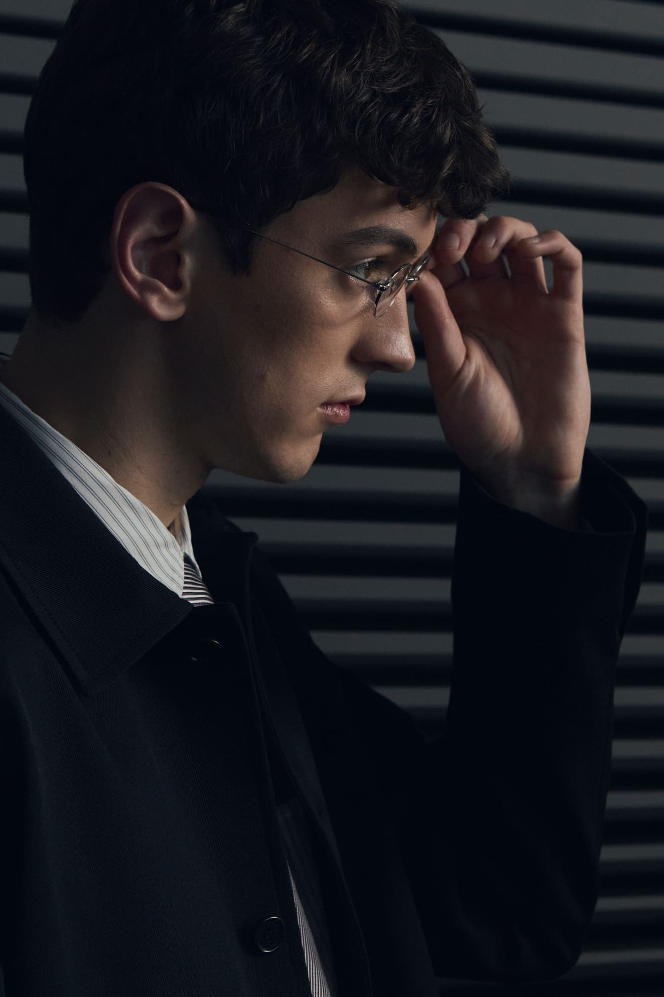A man in a dark coat adjusting his glasses in low light