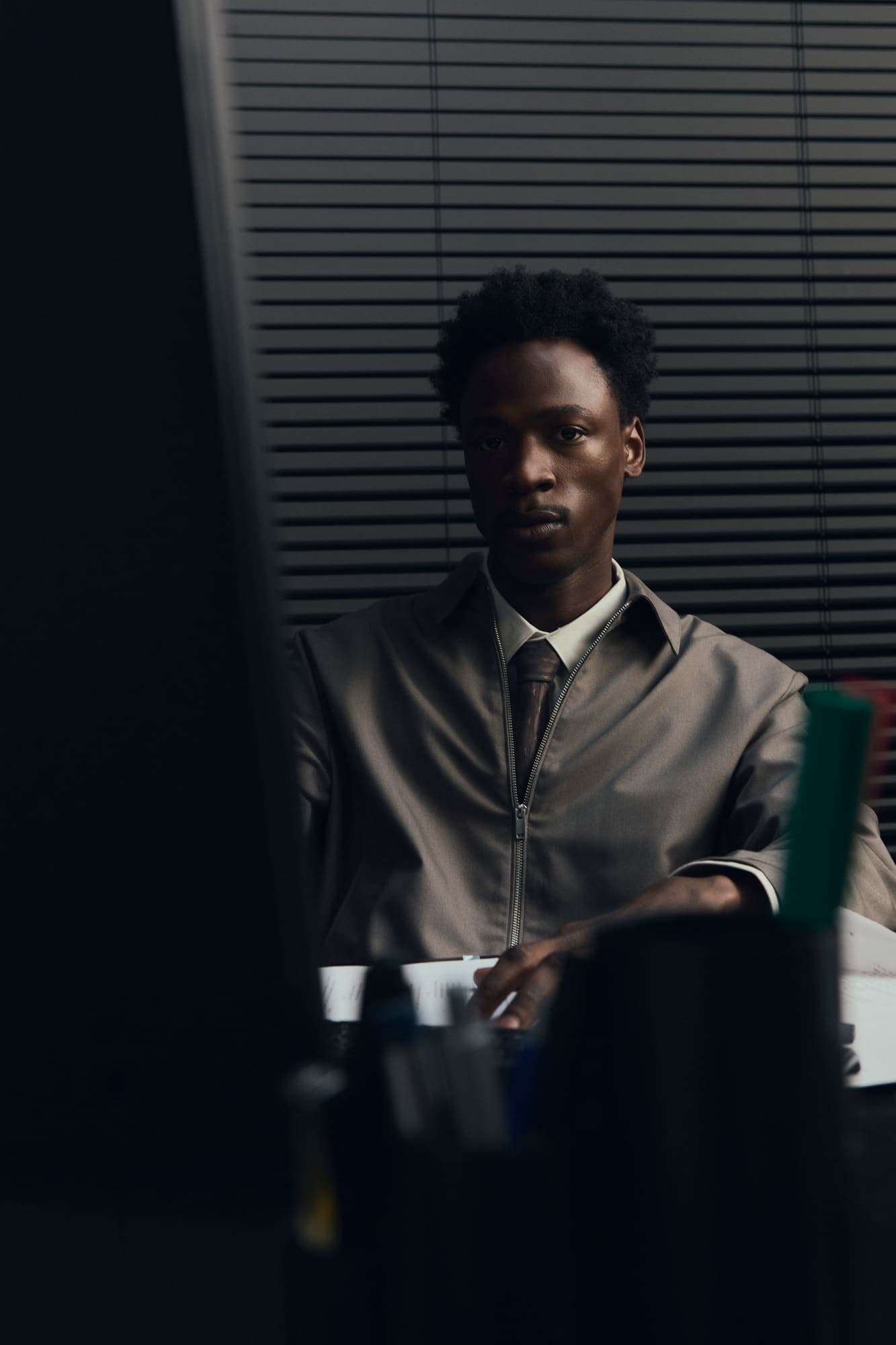 An analyst in a grey jacket staring past a monitor in a dark office at night