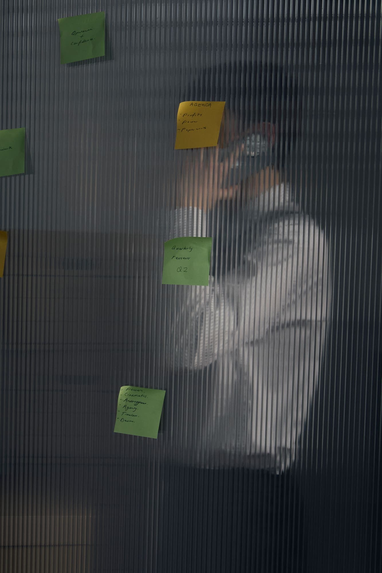 A figure taking a phone call behind reeded glass scattered with sticky notes