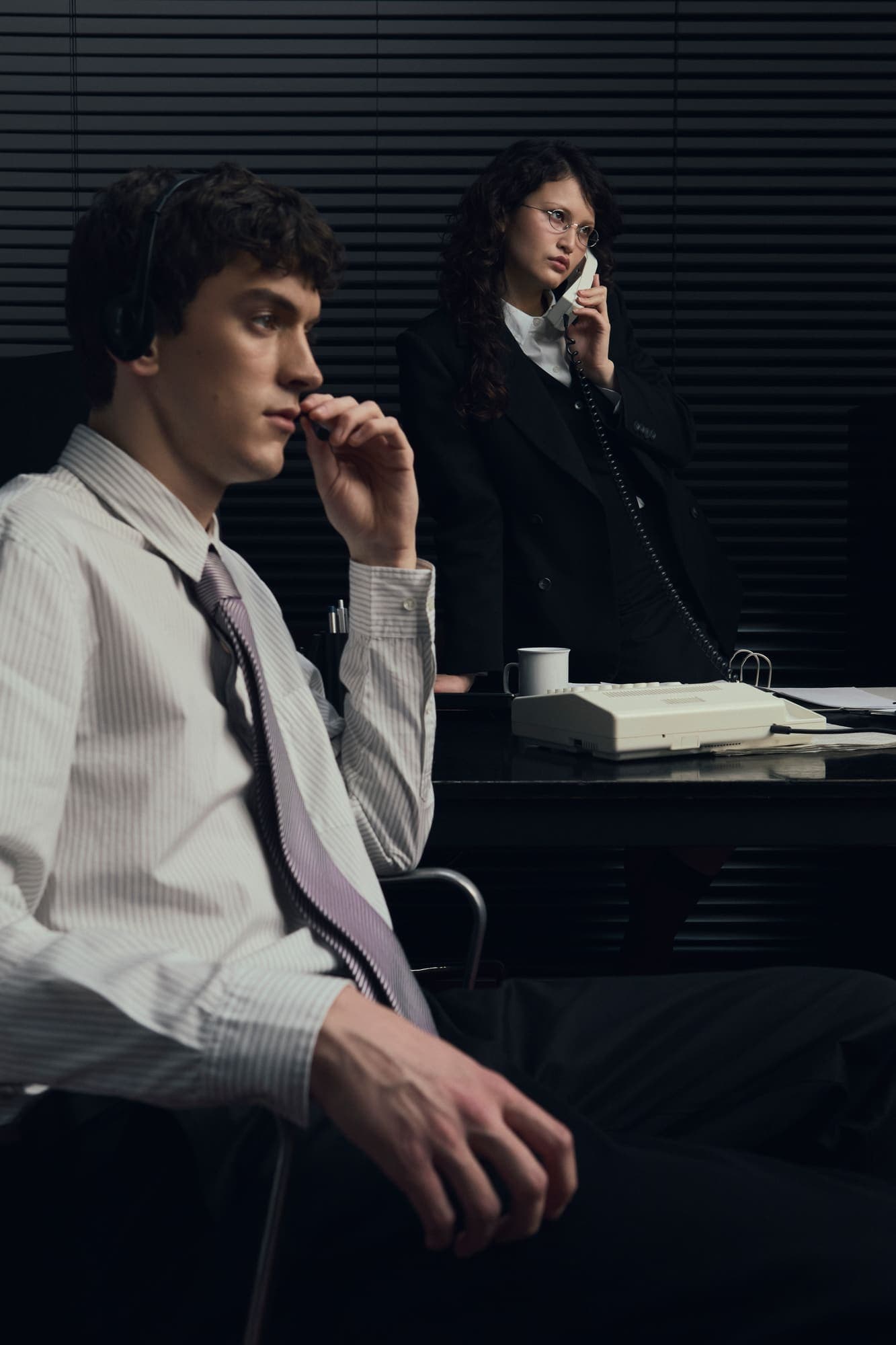 A seated man listening while a colleague behind him takes a phone call
