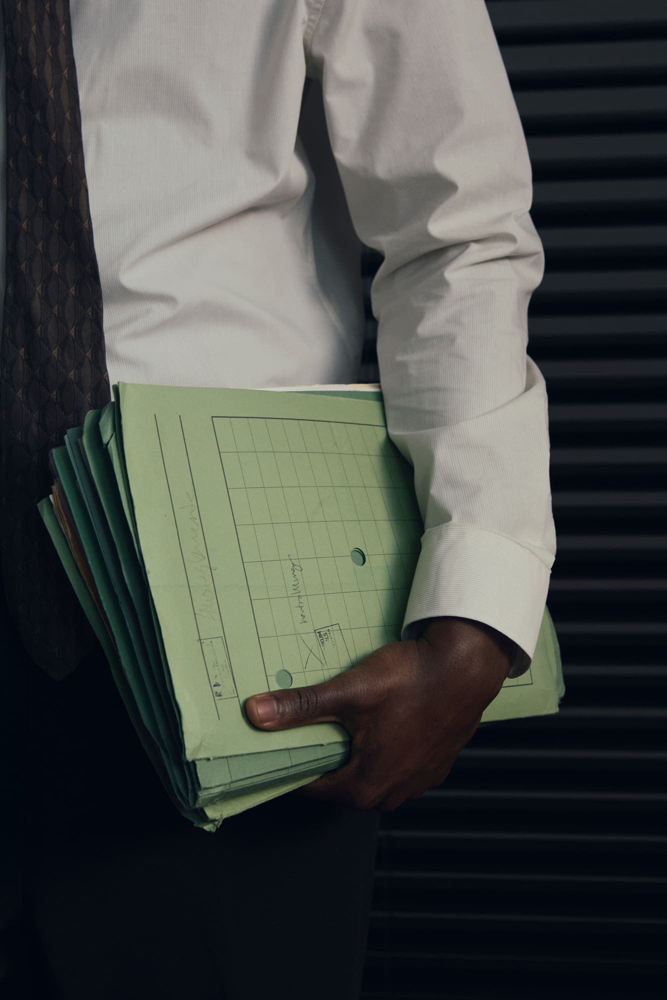 A man carrying a stack of green ledger folders under one arm
