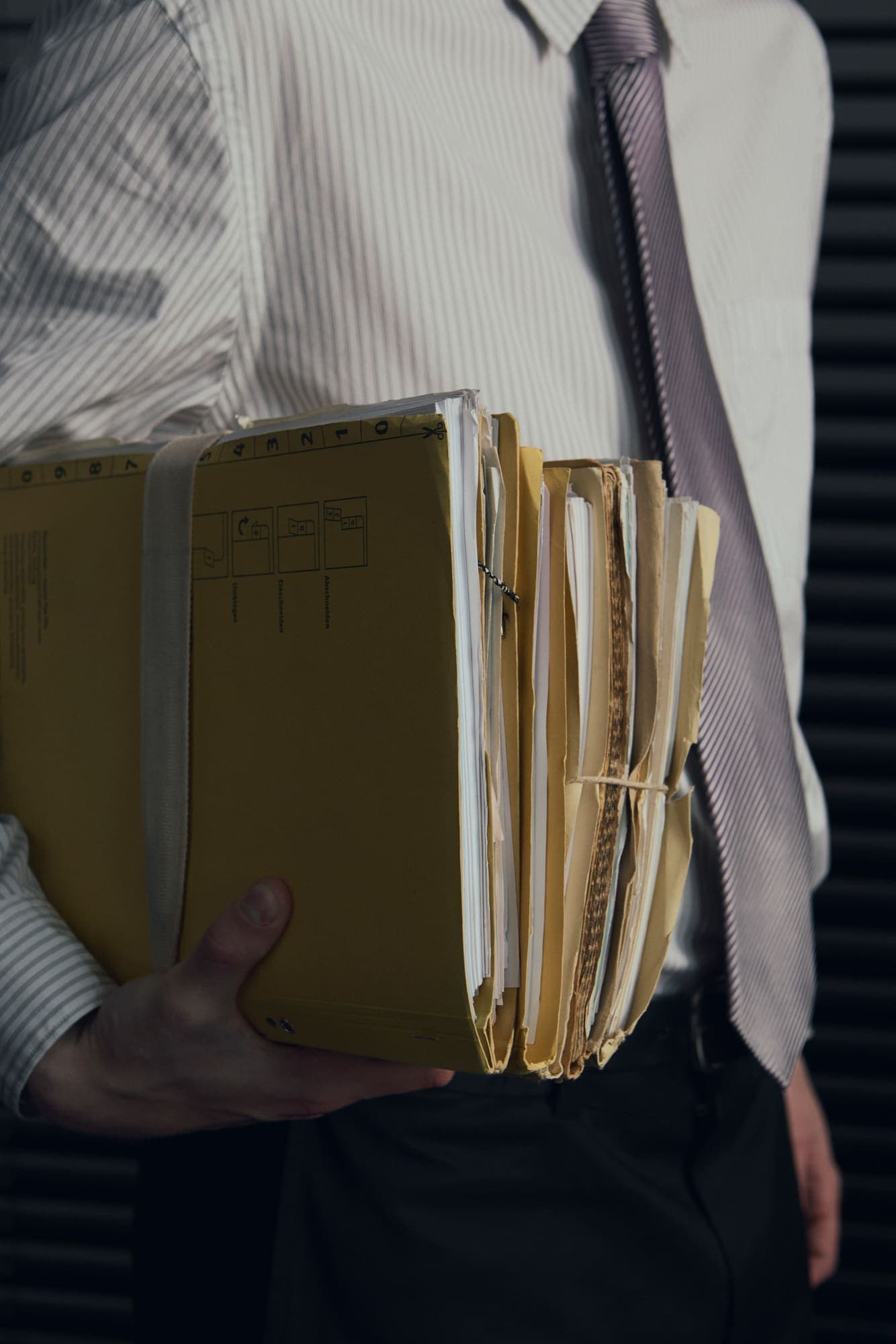 A person carrying a bundle of yellow document folders under one arm