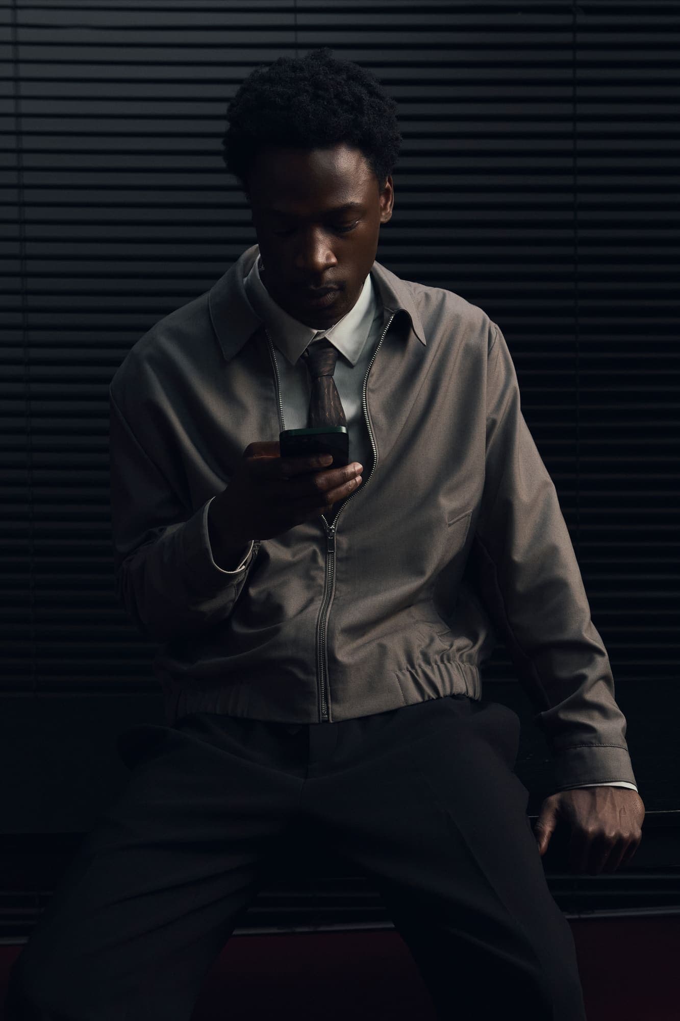A man in a beige jacket checking his mobile phone in a dark office