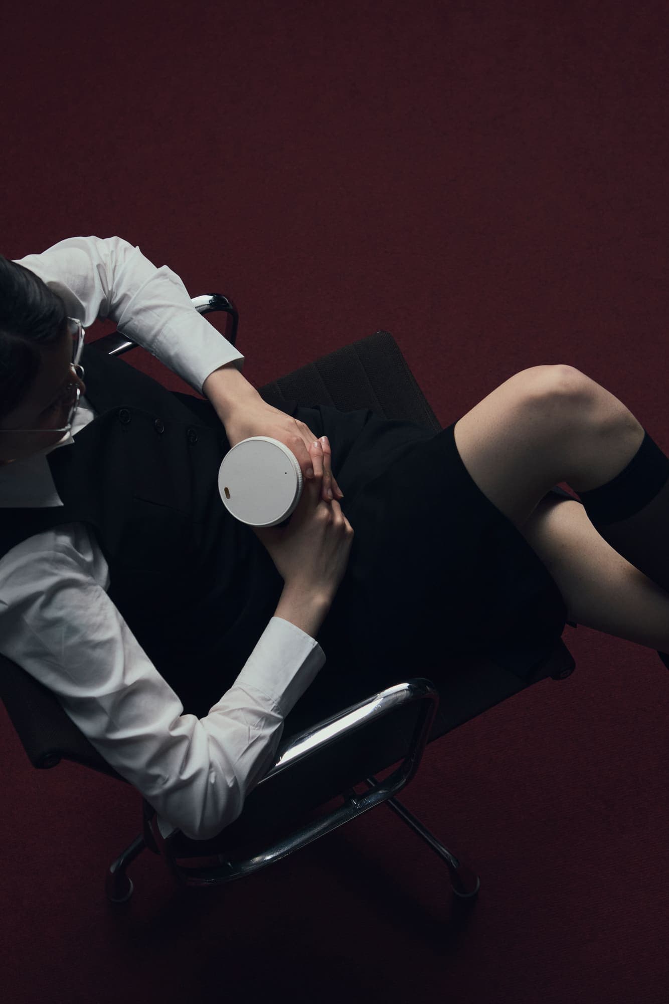 Overhead view of a woman reclining in an office chair holding a white coffee cup