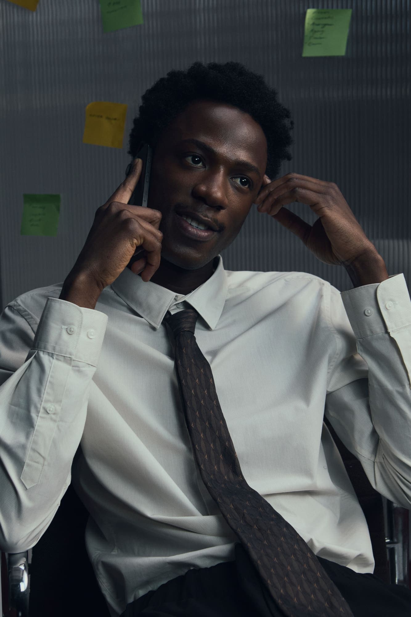 A man in shirt and tie taking a confident phone call in front of sticky-noted glass