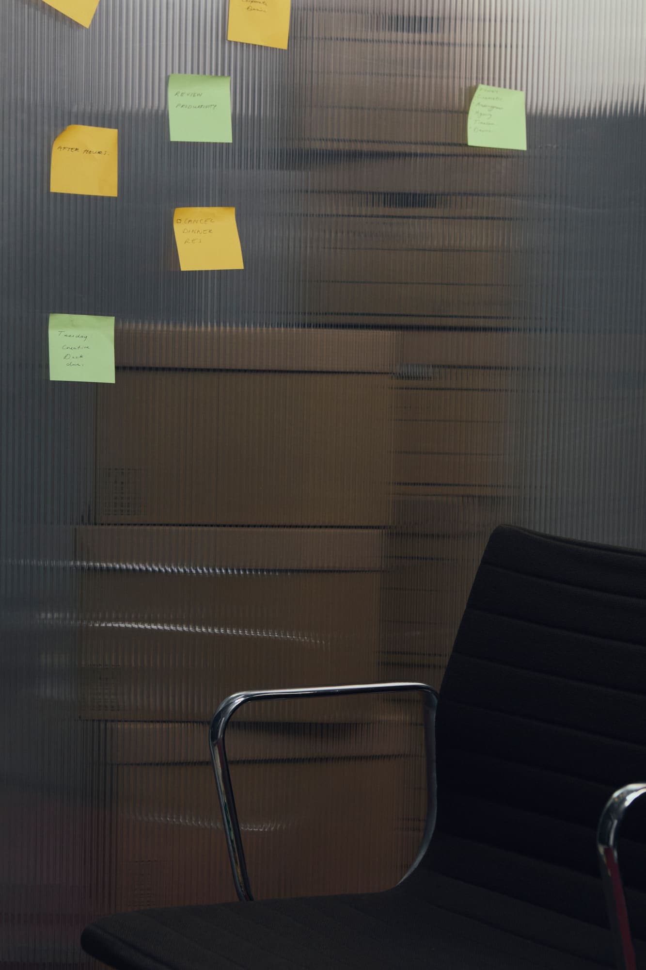 An empty office chair behind reeded glass covered in sticky notes, boxes stacked behind