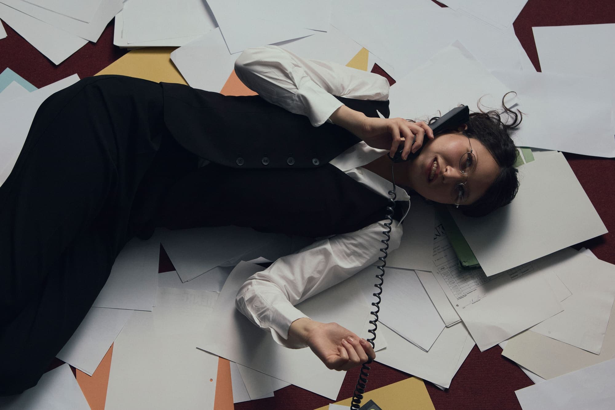 A woman lying on a paper-covered floor taking a call on a corded phone