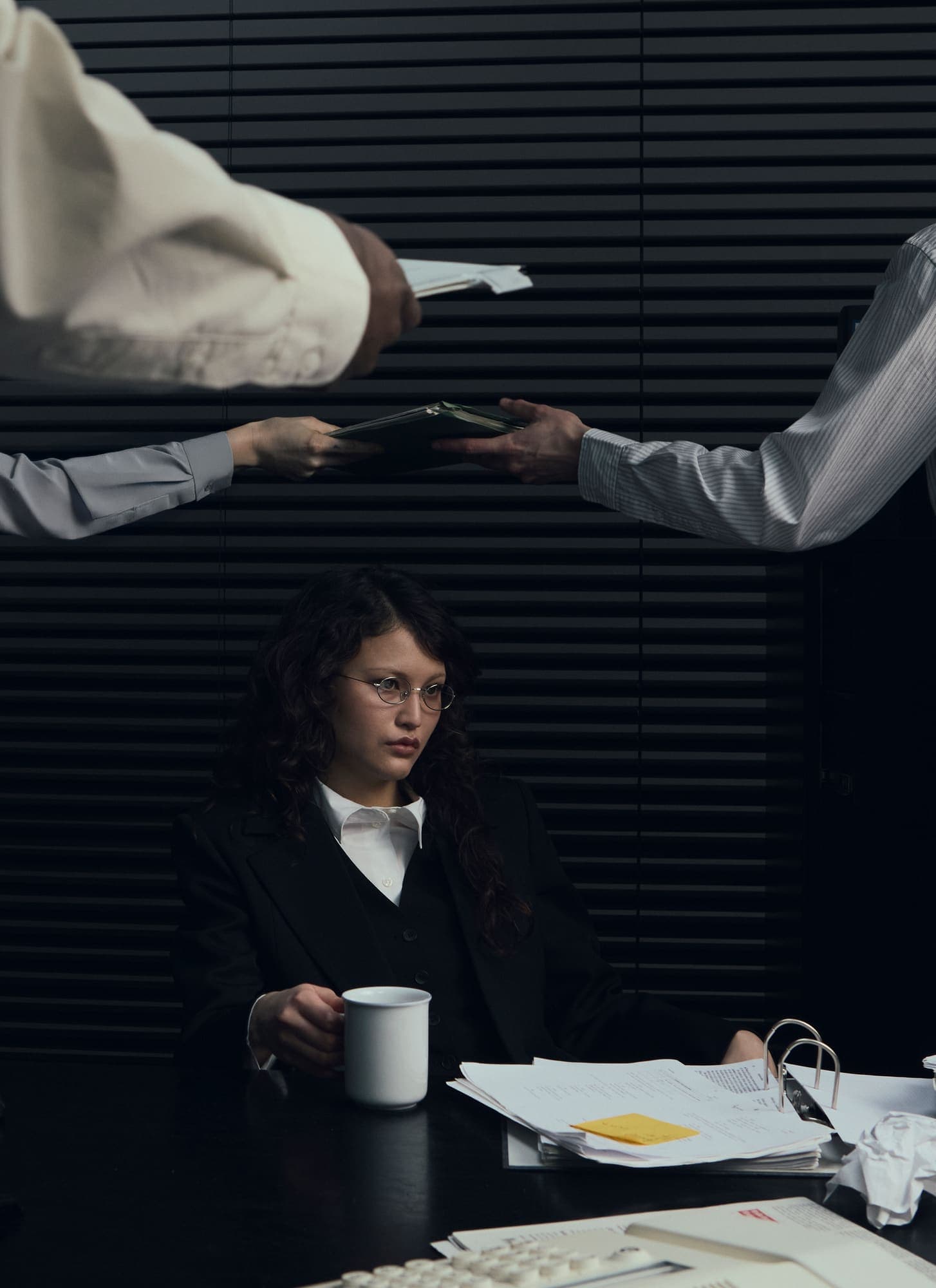 Two colleagues passing a file over a desk while a woman with a mug looks on
