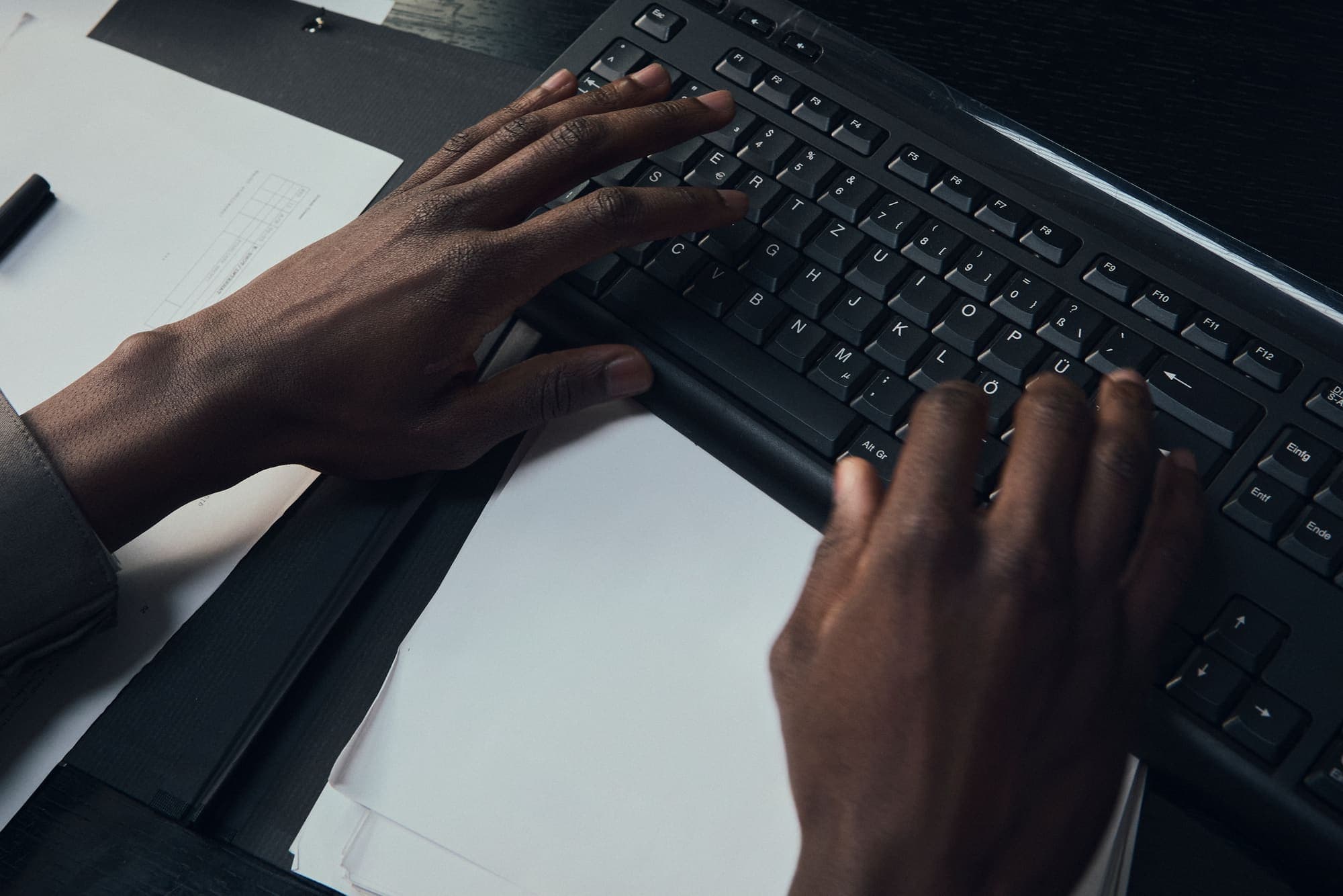 Close-up of hands typing on a black keyboard over paperwork at night