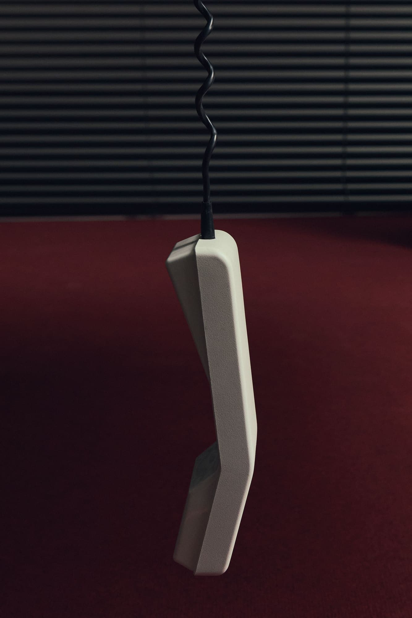 A phone handset dangling by its cord above an oxblood-red carpet