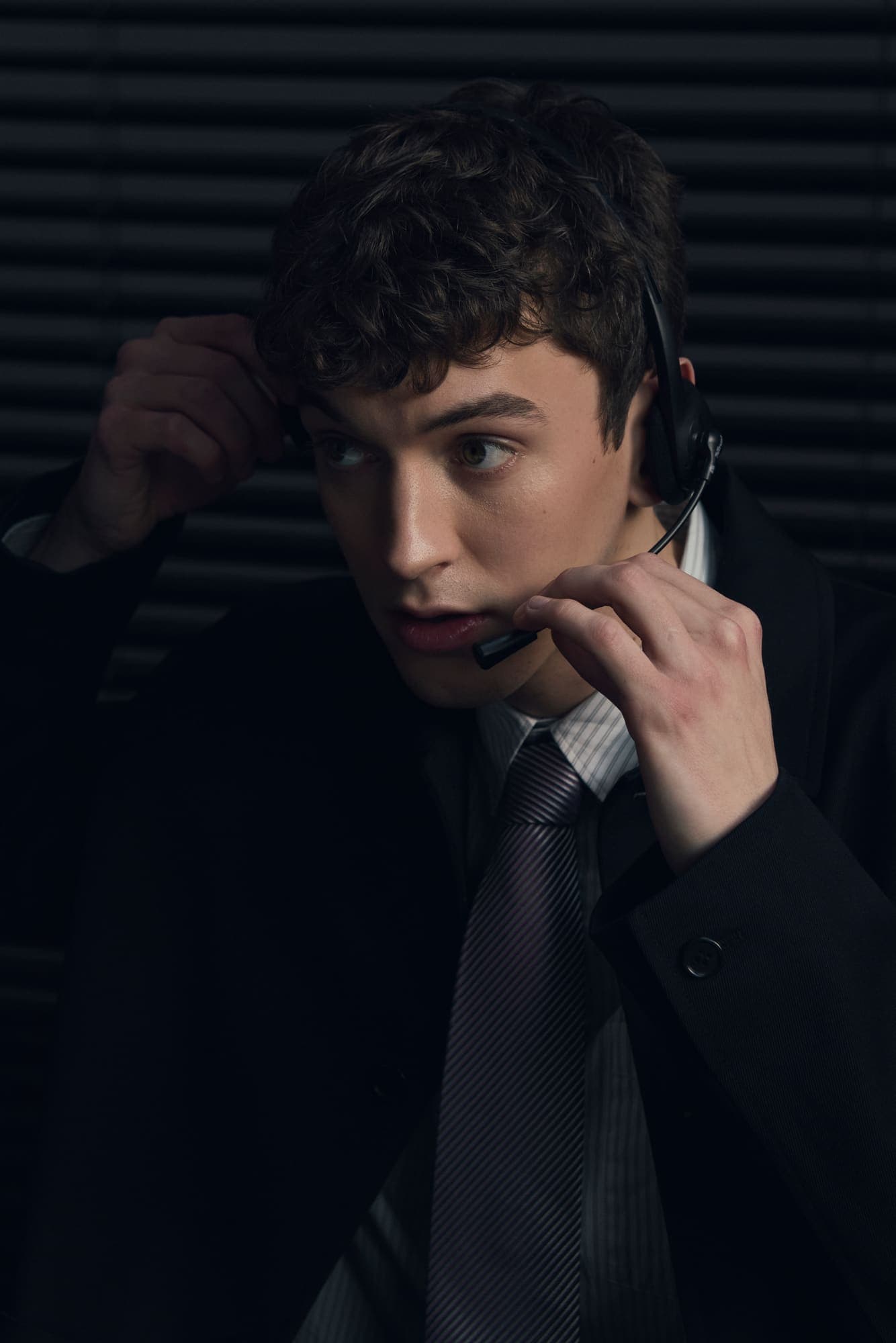 A young man adjusting a telephone headset mid-call, glancing to the side