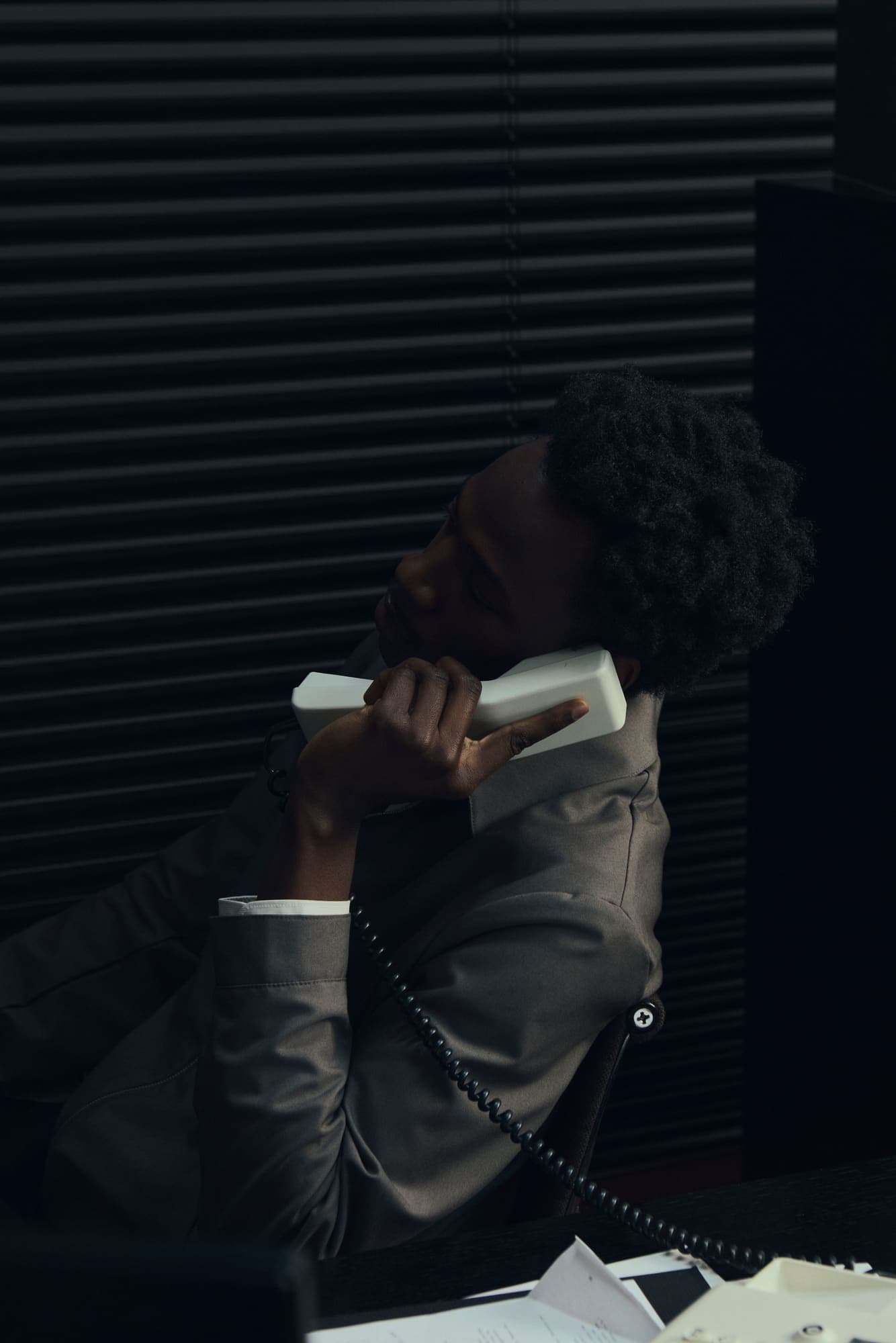 A man hunched over a corded phone taking a hushed call in a dark office
