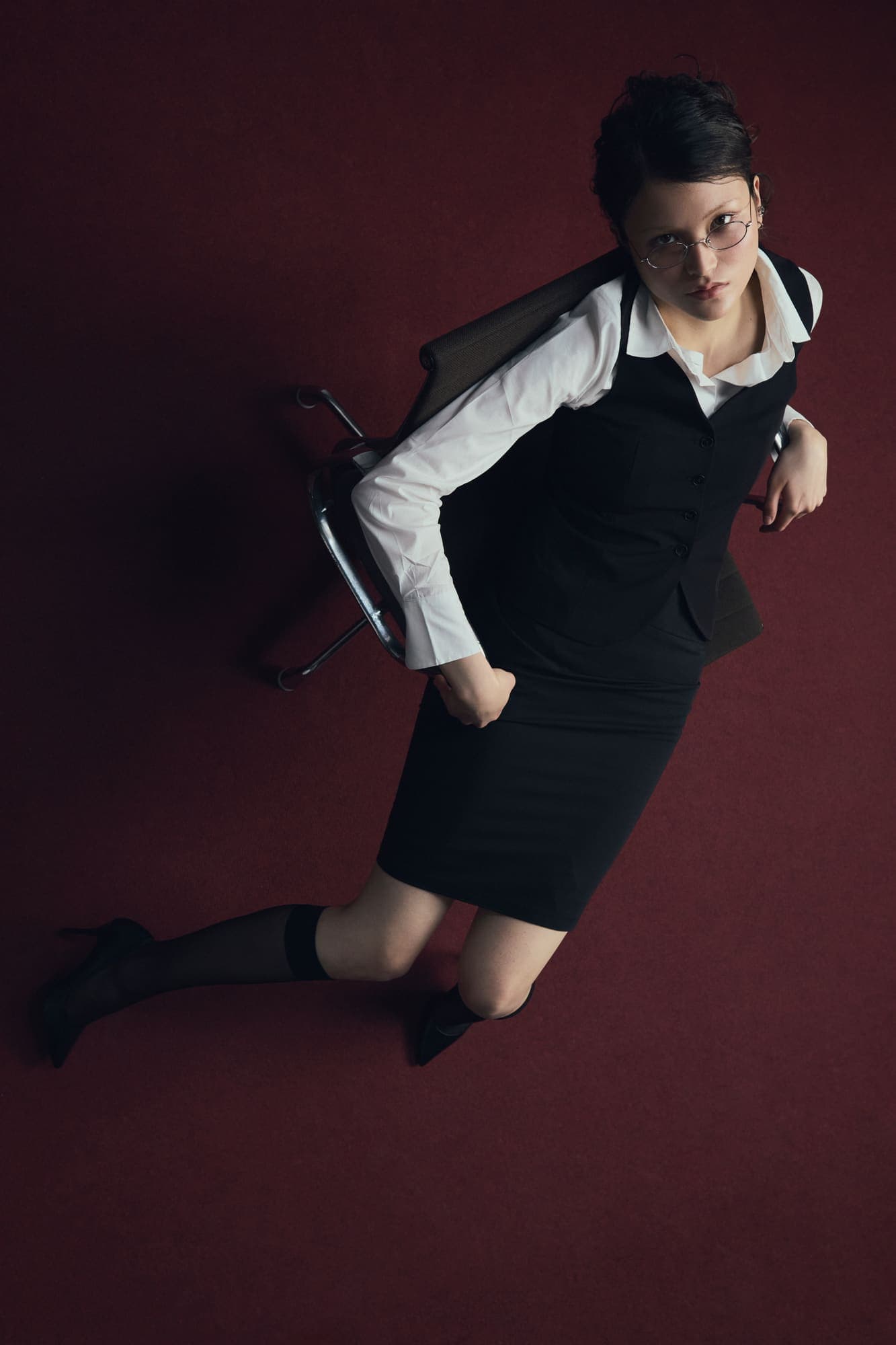 Overhead shot of a woman in a vest and skirt kneeling on red carpet looking up at the camera