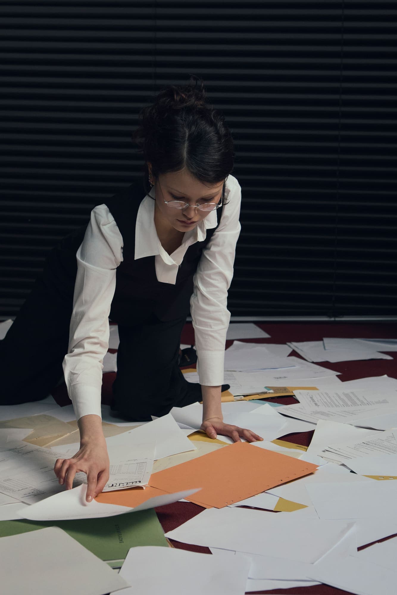 A woman kneeling on a paper-covered floor sorting pages into piles