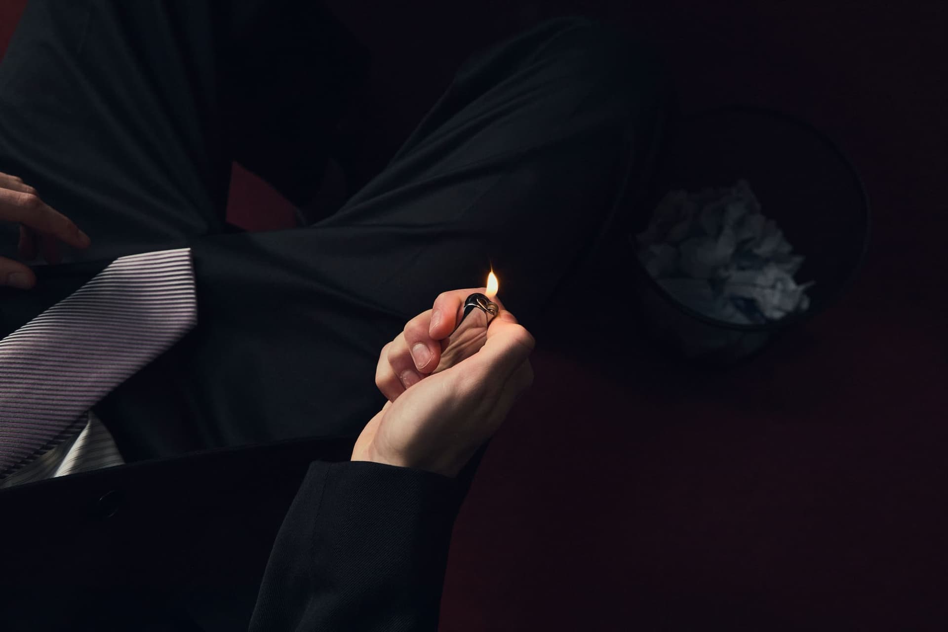 A hand flicking a lighter in deep shadow beside a wastepaper basket