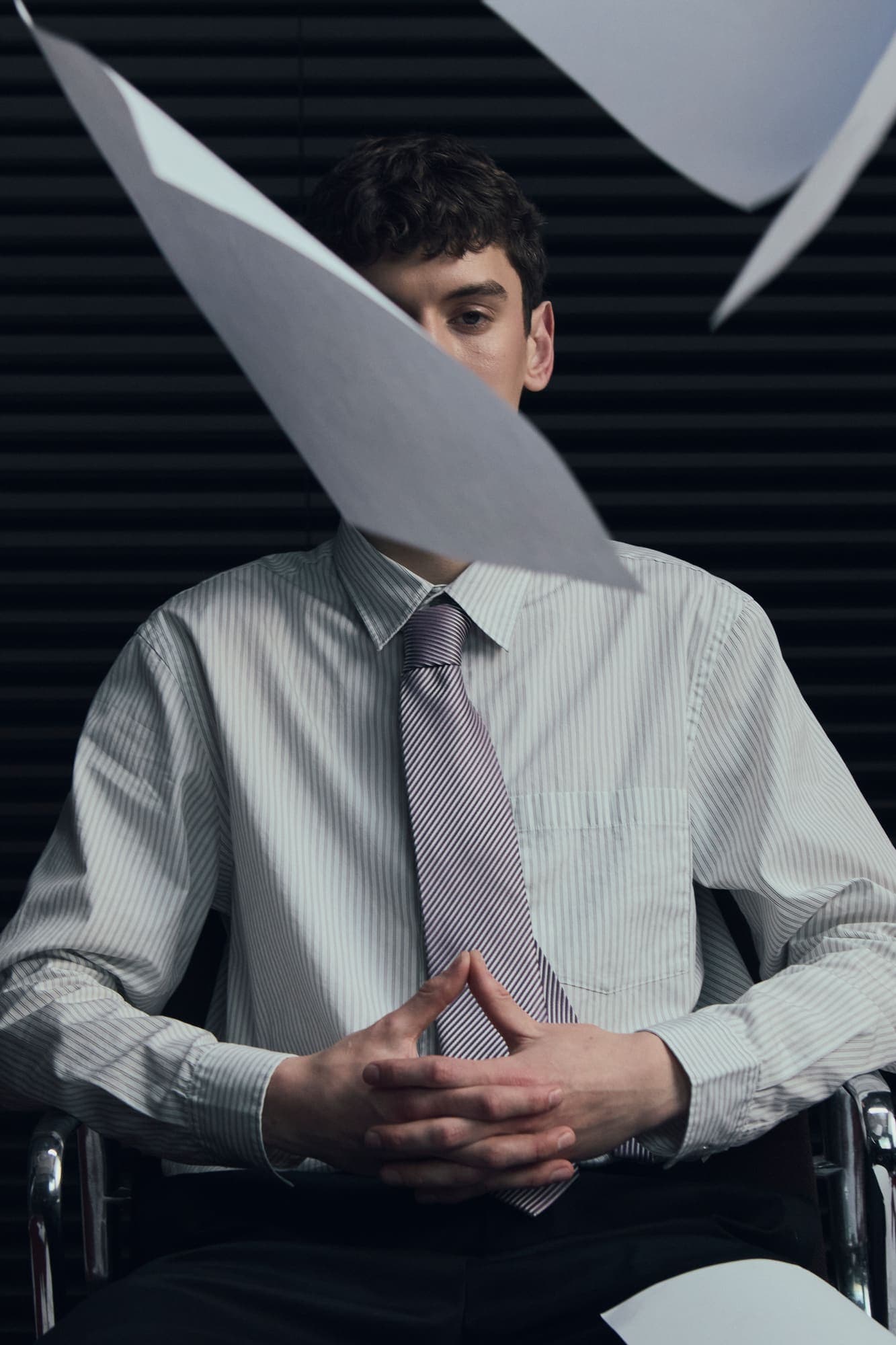A sheet of falling paper covering the face of a seated man in shirt and tie
