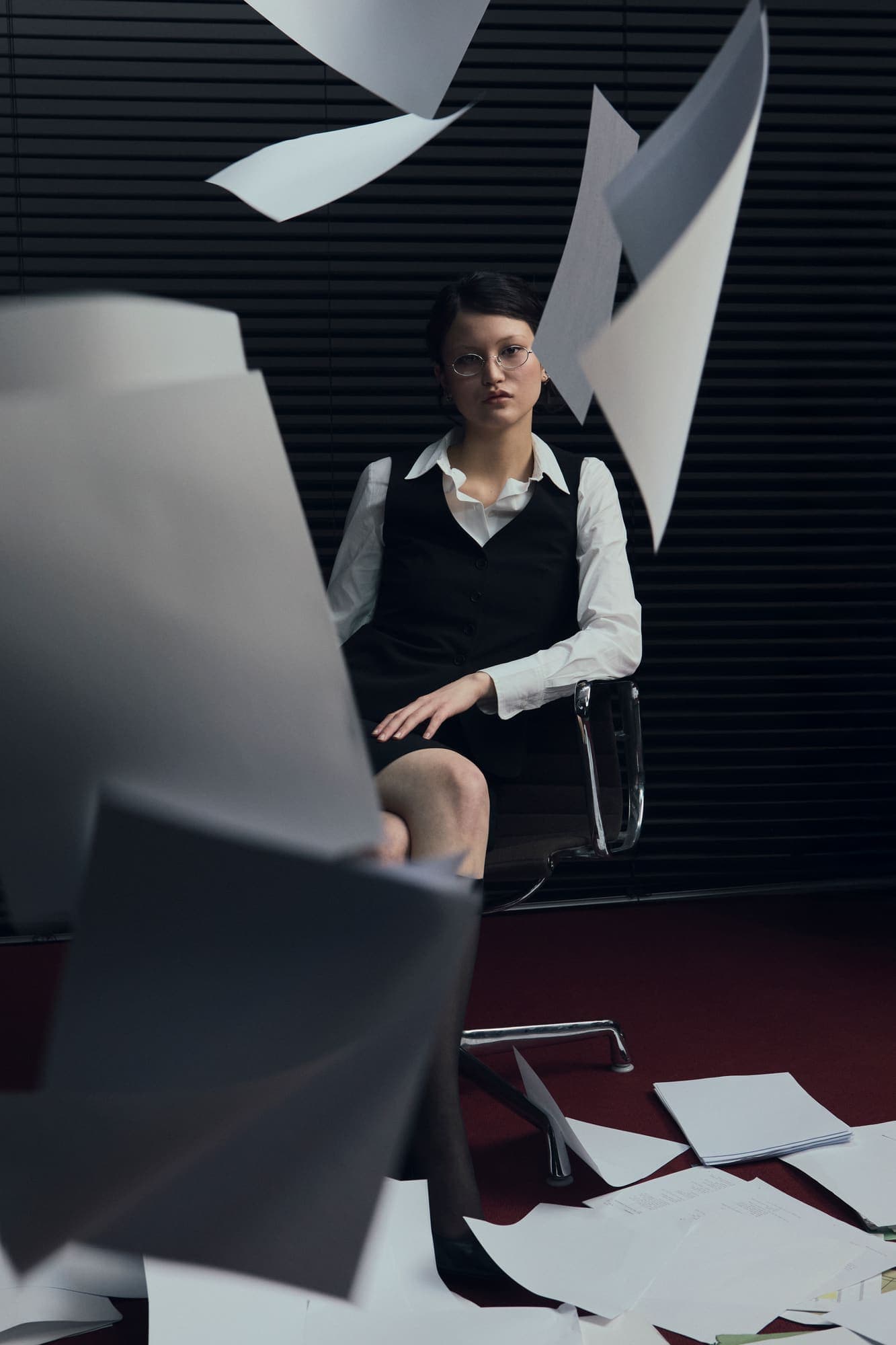 A woman seated calmly in an office chair as printed pages fall around her