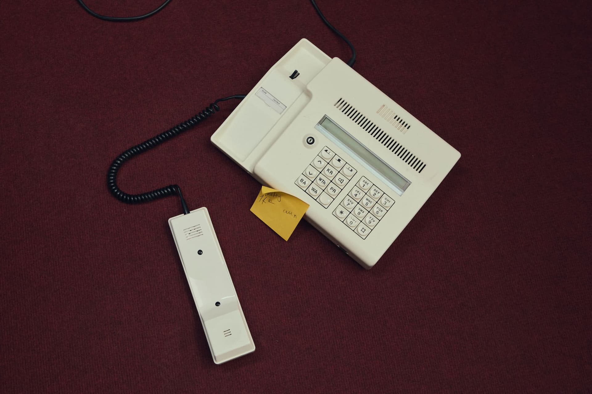 A corded desk phone with a sticky note resting on an oxblood-red carpet