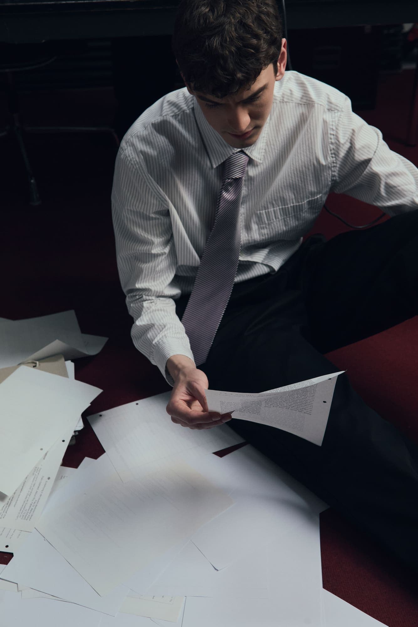 A man seated on the floor sorting through scattered printed reports