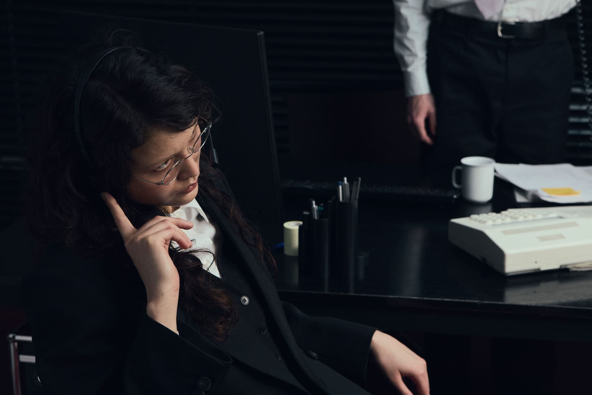 A woman leaning back mid-call while a colleague stands behind her desk