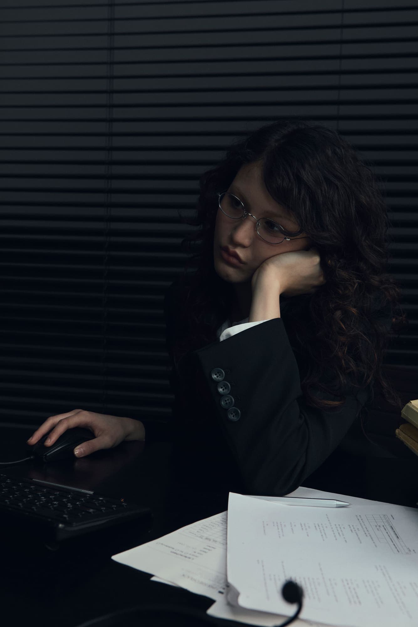 A woman resting her head on one hand while working at a dark terminal late at night